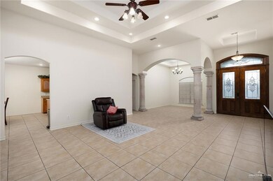 Foyer with french doors, ceiling fan with notable chandelier, ornate columns, and light tile patterned flooring