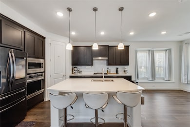 Kitchen with stainless steel appliances, dark brown cabinetry, hanging light fixtures, and recessed lighting