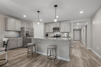 Kitchen featuring gray cabinets, stainless steel appliances, a kitchen breakfast bar, light stone countertops, and recessed lighting