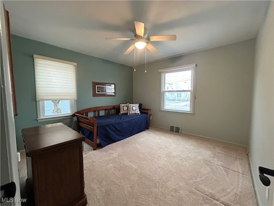 Carpeted bedroom on first floor with ceiling fan and baseboards