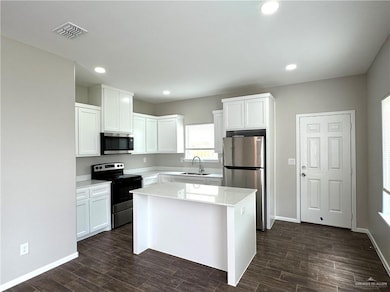 Kitchen featuring stainless steel appliances, white cabinets, a sink, dark wood finished floors, and light countertops