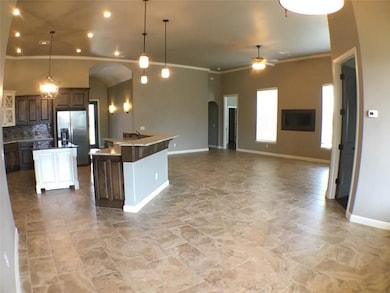 Kitchen with arched walkways, stainless steel fridge with ice dispenser, ceiling fan, ornamental molding, and an island with sink