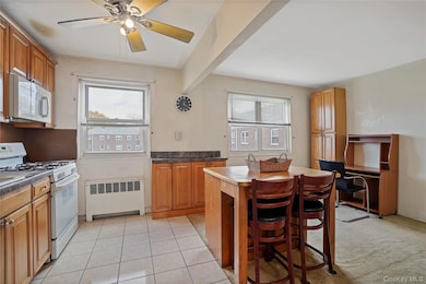 Kitchen featuring white appliances, radiator heating unit, dark countertops, light tile patterned floors, and a kitchen breakfast bar