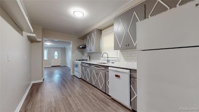 Kitchen featuring white appliances, backsplash, light wood-style flooring, gray cabinets, and ornamental molding