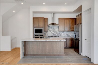 Kitchen with visible vents, appliances with stainless steel finishes, wall chimney exhaust hood, tasteful backsplash, and a center island with sink