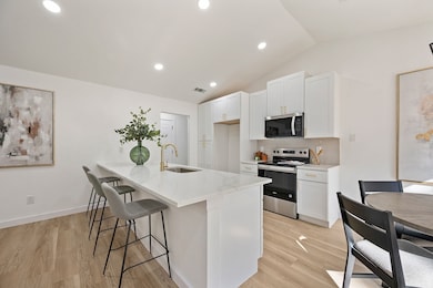 Kitchen featuring appliances with stainless steel finishes, white cabinetry, light stone countertops, lofted ceiling, and light wood-style floors