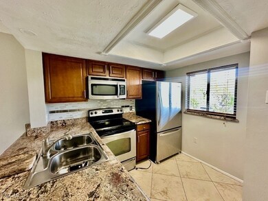 Kitchen with stainless steel appliances, backsplash, light tile patterned flooring, light stone countertops, and a tray ceiling
