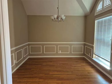Unfurnished dining area featuring a decorative wall, lofted ceiling, a chandelier, wood finished floors, and wainscoting