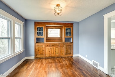 Unfurnished dining area featuring dark hardwood floors, textured ceiling, updated light fixtures, and built-in cabinetry.