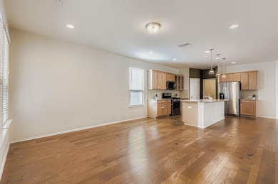 Kitchen with open floor plan, decorative light fixtures, light wood-style floors, appliances with stainless steel finishes, and recessed lighting
