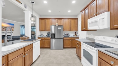 Kitchen with white appliances, brown cabinetry, light countertops, recessed lighting, and decorative light fixtures