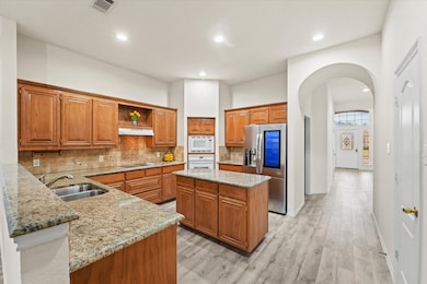 Kitchen with brown cabinetry, backsplash, open shelves, arched walkways, and recessed lighting