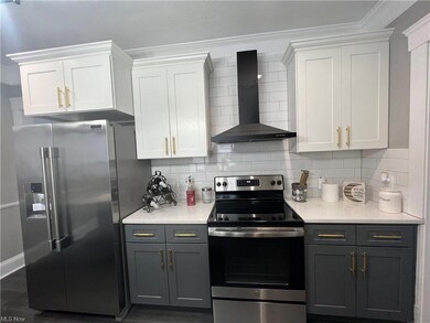 Kitchen featuring appliances with stainless steel finishes, wall chimney exhaust hood, backsplash, white cabinetry, and ornamental molding