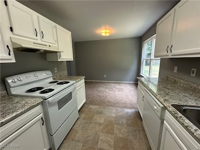 Kitchen with white appliances, under cabinet range hood, white cabinets, and stone finish floors