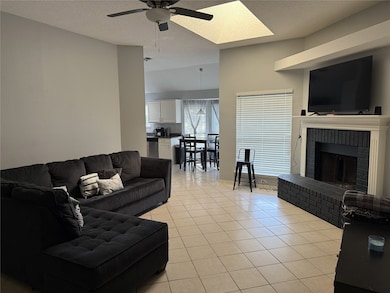 Living area with light tile patterned floors, a textured ceiling, a brick fireplace, ceiling fan, and a skylight