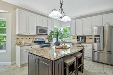 Kitchen featuring appliances with stainless steel finishes, white cabinets, light stone counters, a center island, and decorative backsplash