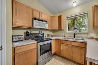 Kitchen featuring stainless steel electric range oven, a textured ceiling, white microwave, light countertops, and lofted ceiling