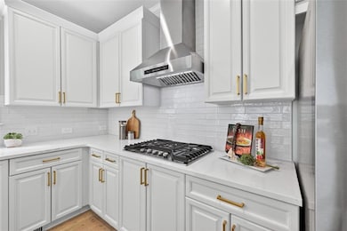 Kitchen featuring wall chimney range hood, white cabinets, decorative backsplash, and light stone counters