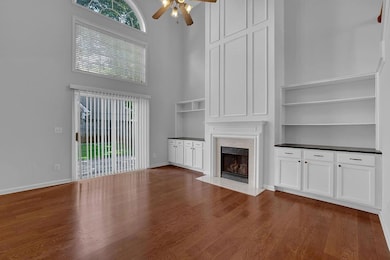 Unfurnished living room with a towering ceiling, a ceiling fan, dark wood-type flooring, healthy amount of natural light, and a high end fireplace
