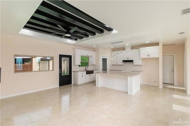 Kitchen featuring backsplash, white cabinetry, under cabinet range hood, a center island, and light stone counters