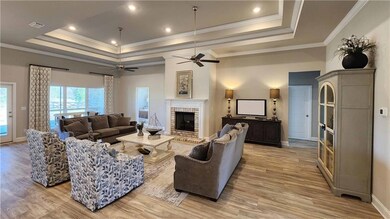 Living area with a tray ceiling, a fireplace, crown molding, light wood-style floors, and recessed lighting