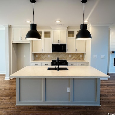 Kitchen featuring decorative backsplash, light stone countertops, dark wood-style flooring, hanging light fixtures, and crown molding