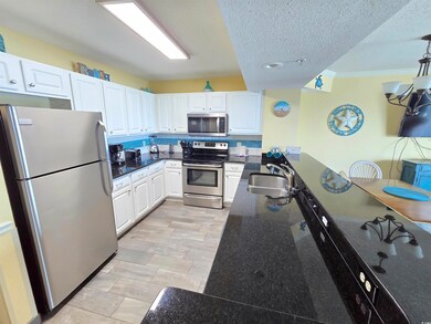 Kitchen featuring stainless steel appliances, white cabinets, dark stone counters, crown molding, and a textured ceiling