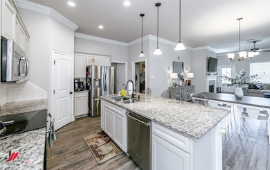 Kitchen featuring appliances with stainless steel finishes, open floor plan, a chandelier, crown molding, and white cabinets