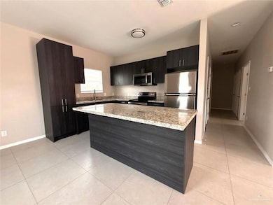 Kitchen with appliances with stainless steel finishes, a kitchen island, light tile patterned floors, dark cabinets, and light stone countertops
