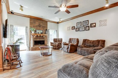 Living room with light wood-type flooring, crown molding, ceiling fan, a fireplace, and a textured ceiling