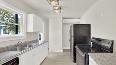 Kitchen featuring electric range, white cabinets, light wood-type flooring, light countertops, and dishwasher