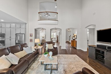 View back toward the front of the home. Notice the lovely Juliet balcony off the upstairs game room, and the pretty pendant lighting framing the arches underneath. On the far right is a well-appointed powder room.