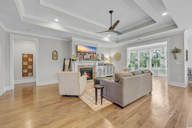 Living room with a tray ceiling, a ceiling fan, light wood-style flooring, a fireplace, and recessed lighting