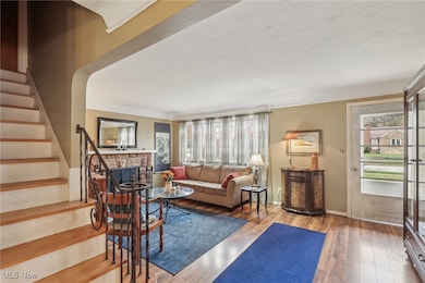 Living room featuring stairway, light wood-style floors, a stone fireplace, and plenty of natural light