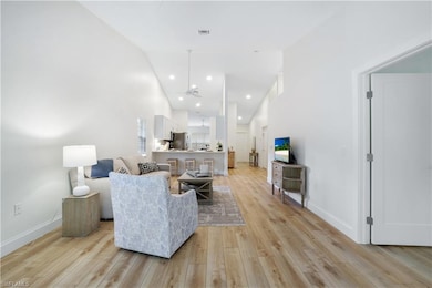 Living area with light wood-style floors, baseboards, high vaulted ceiling, and recessed lighting