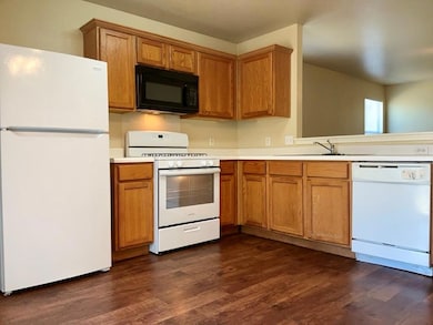 Kitchen featuring white appliances, light countertops, dark wood finished floors, and brown cabinetry