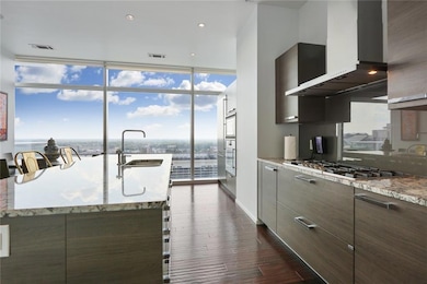 Kitchen with wall chimney range hood, modern cabinets, a sink, stainless steel gas stovetop, and dark wood-type flooring