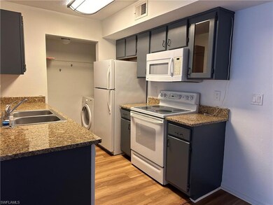 Kitchen featuring light hardwood / wood-style flooring, washer / clothes dryer, dark stone countertops, sink, and white appliances