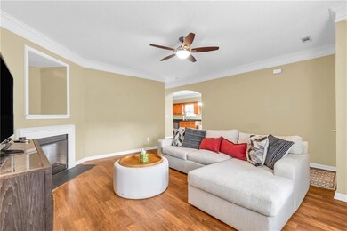 Living area with arched walkways, ceiling fan, ornamental molding, wood finished floors, and a fireplace with flush hearth