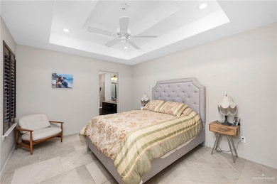 Bedroom featuring a tray ceiling, connected bathroom, ceiling fan, and recessed lighting