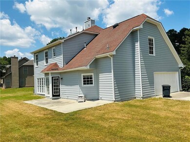 Rear view of house featuring a lawn, a patio area, roof with shingles, a chimney, and driveway