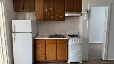 Kitchen with decorative backsplash, white appliances, light countertops, under cabinet range hood, and dark wood-style flooring