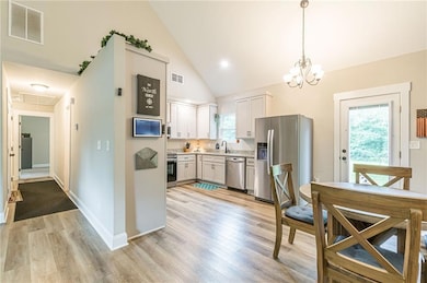 Kitchen with appliances with stainless steel finishes, light countertops, light wood-style floors, pendant lighting, and a chandelier