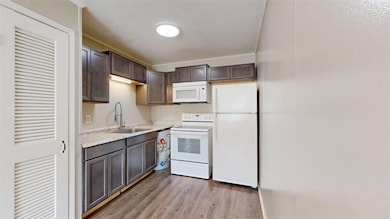 Kitchen with white appliances, dark brown cabinets, light wood-style floors, and ornamental molding