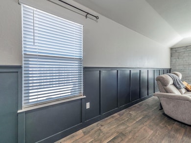 Living area with dark wood-type flooring, wainscoting, a decorative wall, vaulted ceiling, and a textured wall