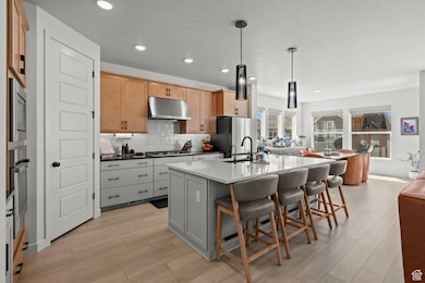 Kitchen with backsplash, a center island with sink, gray cabinets, a kitchen breakfast bar, and decorative light fixtures