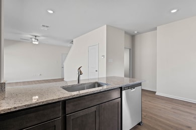 Kitchen with dark wood-style flooring, light stone counters, stainless steel dishwasher, recessed lighting, and dark brown cabinets