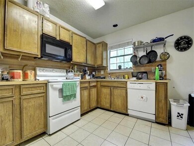 Kitchen with white appliances, light tile patterned floors, a textured ceiling, light countertops, and brown cabinetry