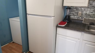 Kitchen featuring freestanding refrigerator, dark countertops, decorative backsplash, white cabinets, and wood finished floors