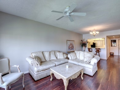 Living room featuring a textured ceiling, dark wood-style flooring, a chandelier, and a ceiling fan
